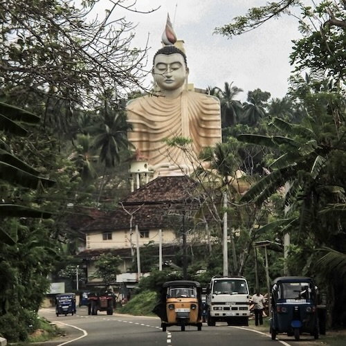 Typical Sri Lankan road with tuk tuk and Buddha statue near Hikkaduwa
